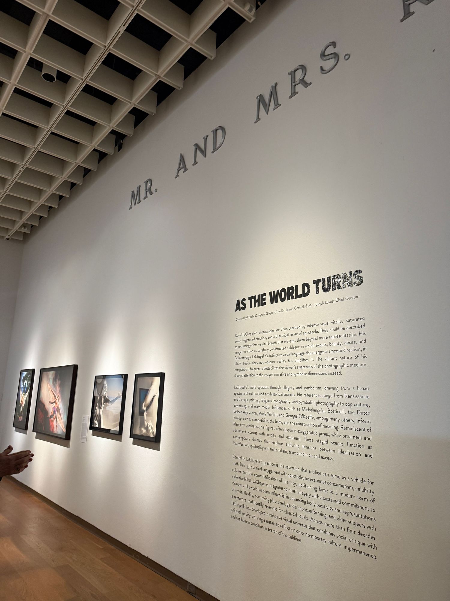 Art gallery interior showing photographs mounted on white walls with text displays and track lighting above.