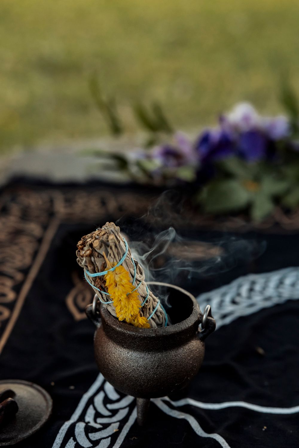 Smoking sage bundle in ritual cauldron with decorative altar cloth.