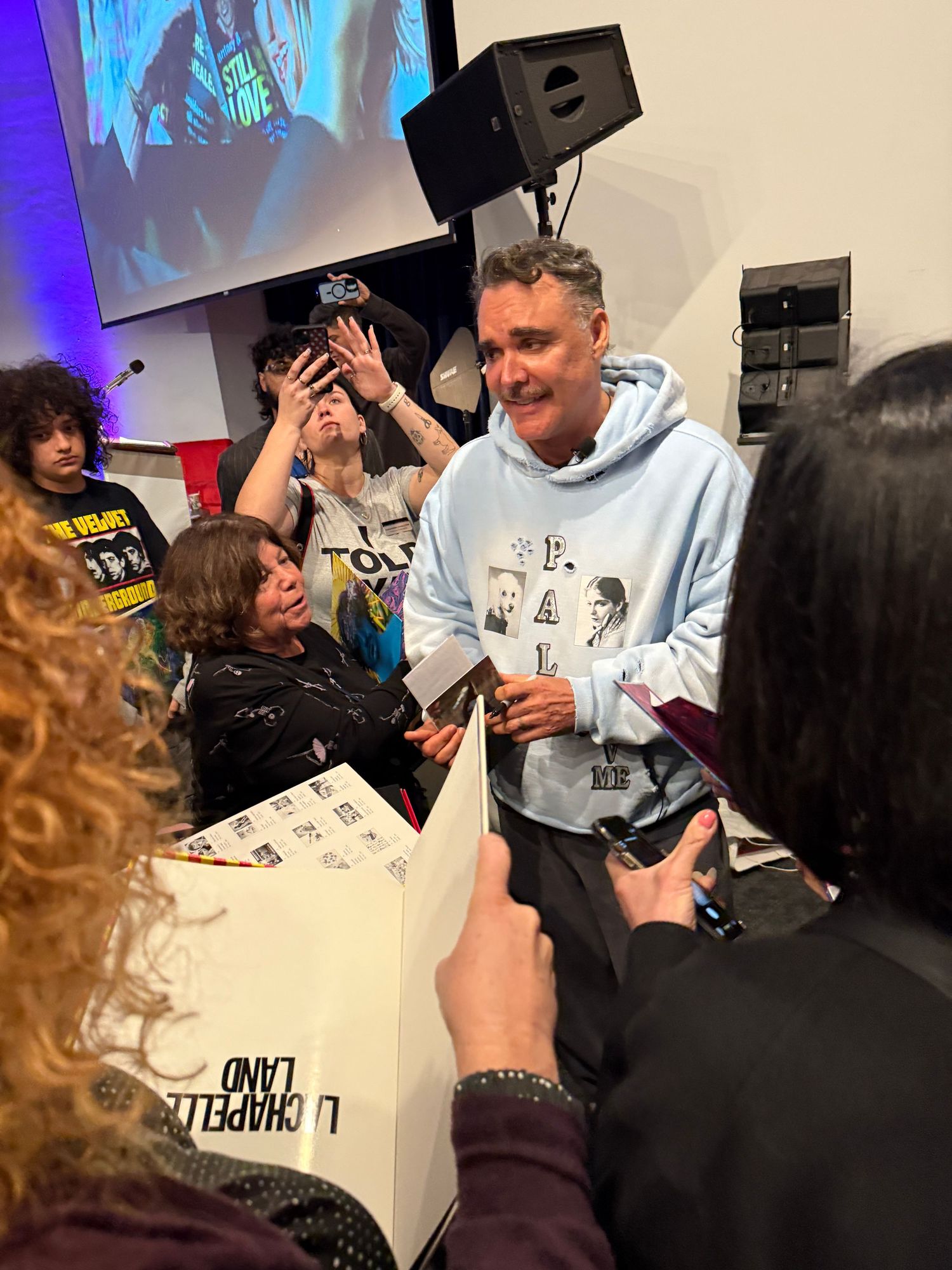 People gathered in an indoor space signing items with markers in a casual setting with blue lighting.