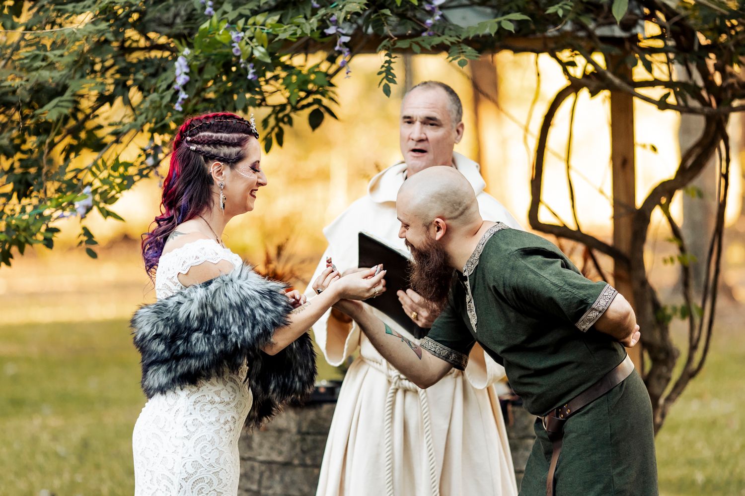 Bride and groom laugh joyfully with officiant during intimate Viking-themed outdoor wedding ceremony.