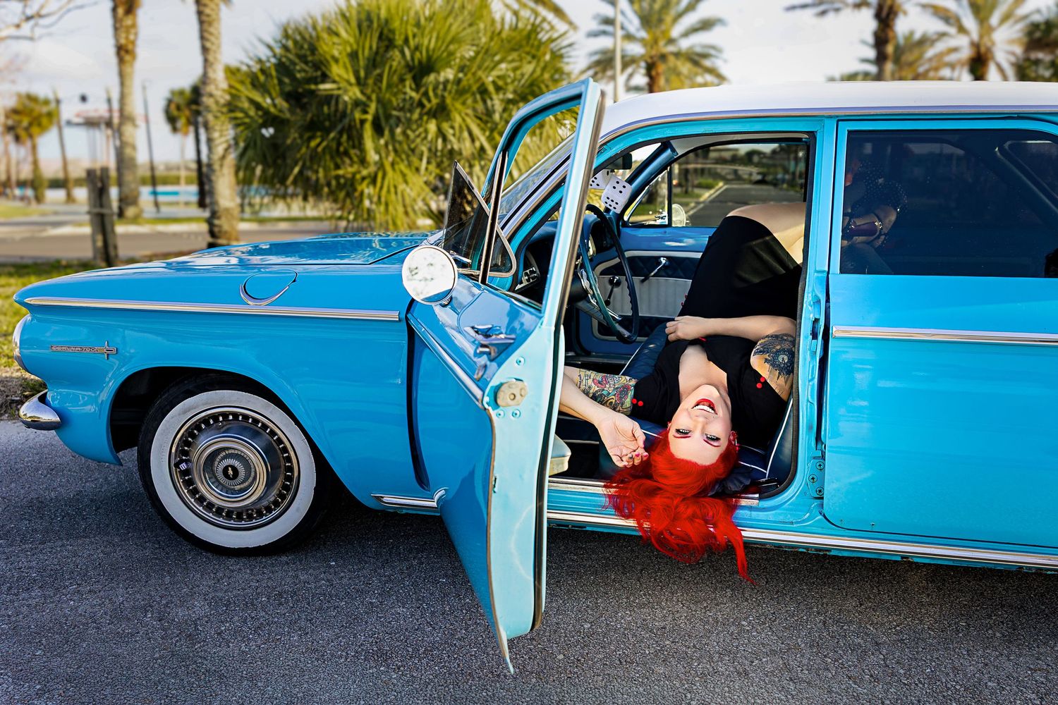 Tattooed redhead pinup model posing in open door of classic blue vintage car.