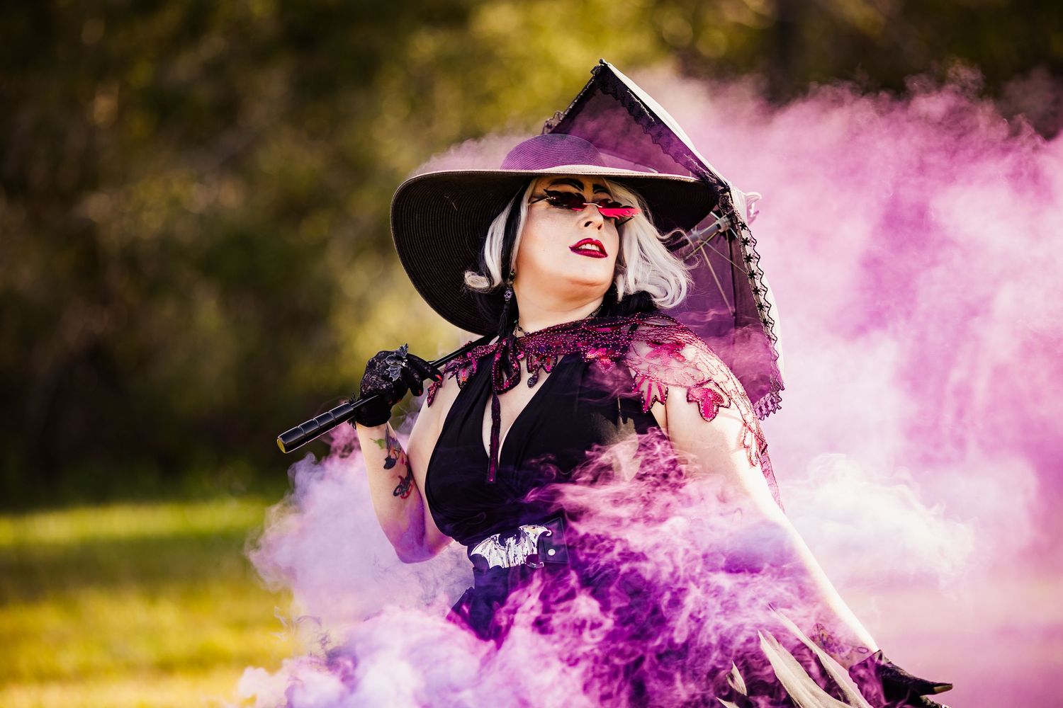 Woman in purple witch hat and black dress surrounded by vibrant purple smoke outdoors.
