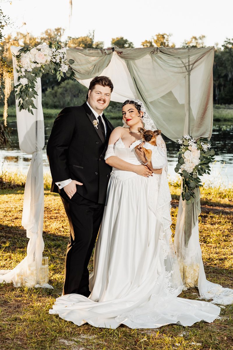 Outdoor wedding ceremony setup with white fabric draping and natural sunset lighting.