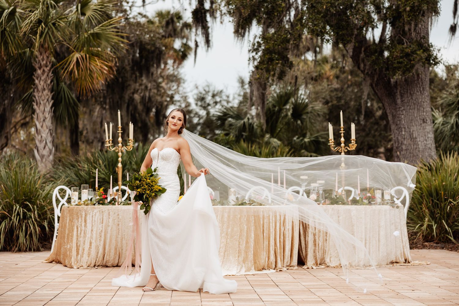 White wedding dress sweeps across elegant outdoor venue with candle-lit table and Spanish moss backdrop.
