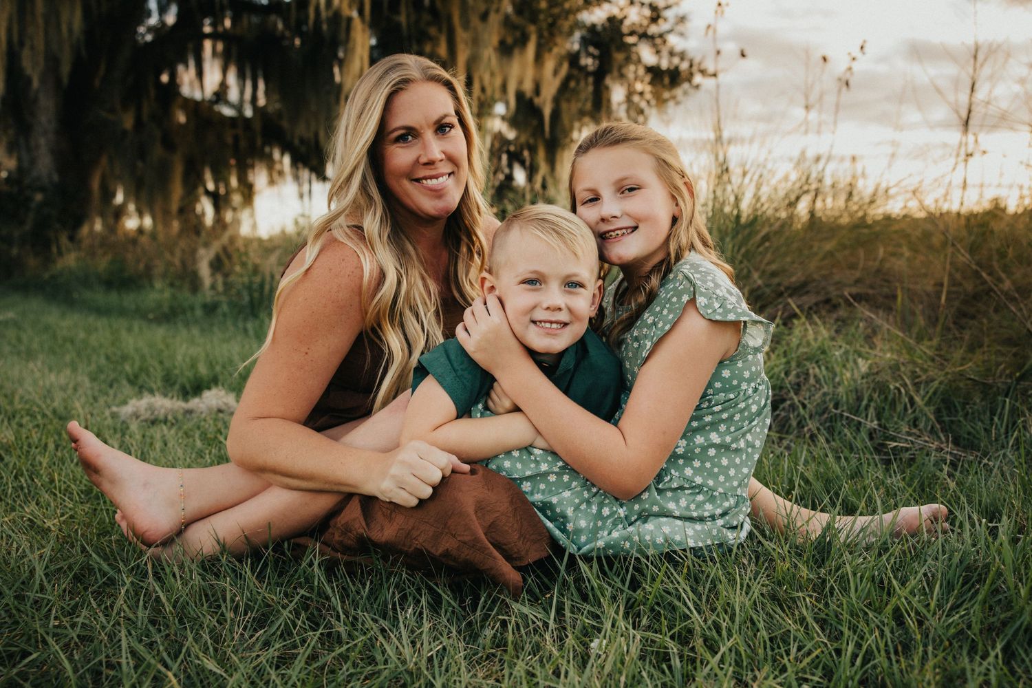A joyful family portrait session on grass with Spanish moss trees at sunset.