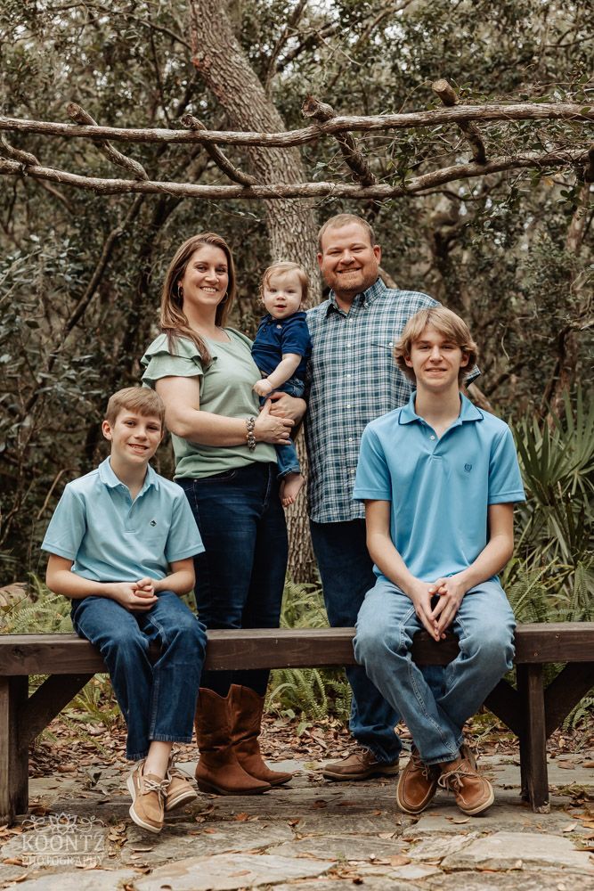 Family portrait on a wooden bench with tropical foliage and trees in the background.