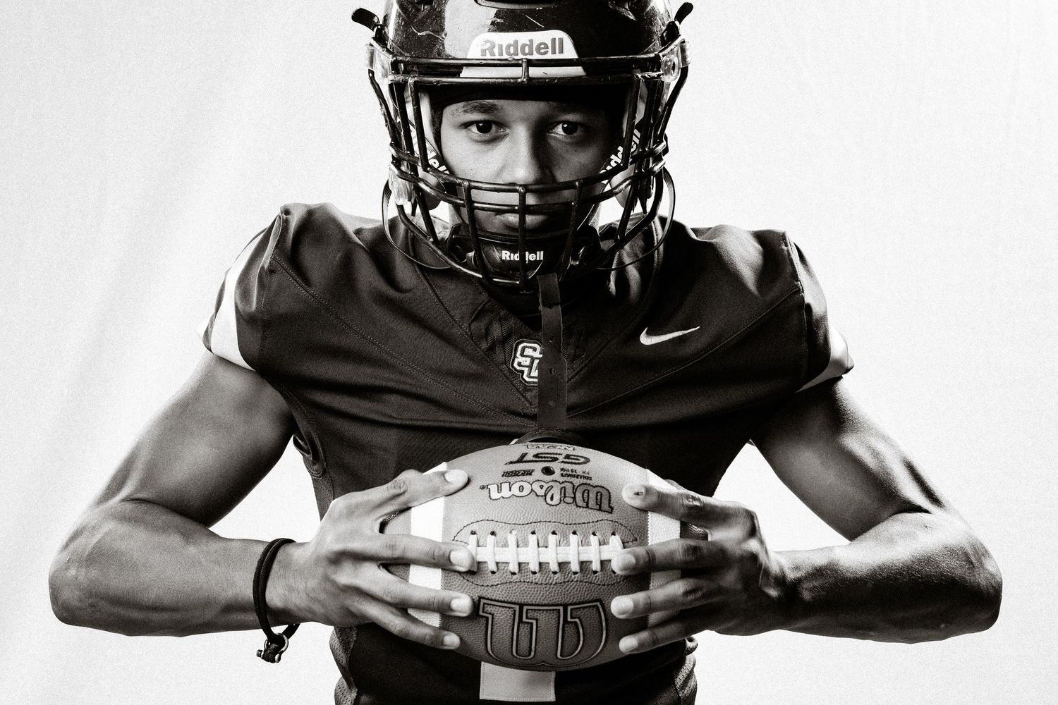Football player poses with ball in stark black and white portrait wearing Nike helmet.