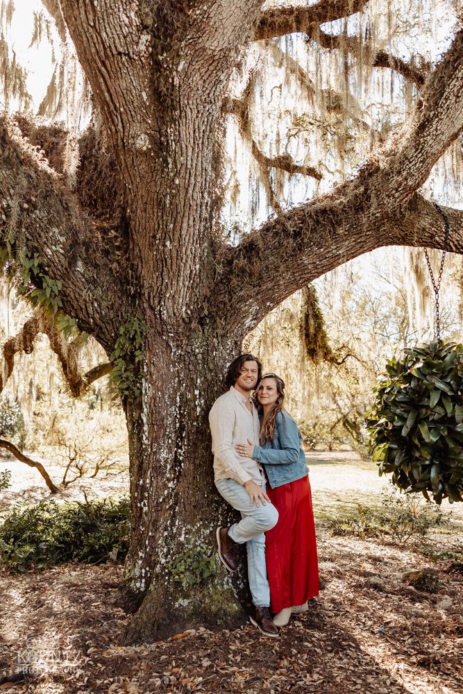 A couple embraces beneath a majestic oak tree draped with Spanish moss.