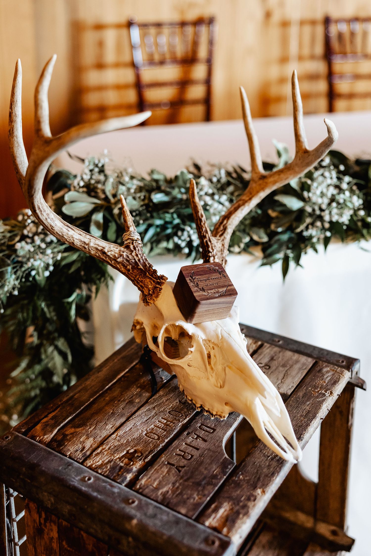Decorative deer skull with antlers displayed on wooden crate with greenery and floral accents.