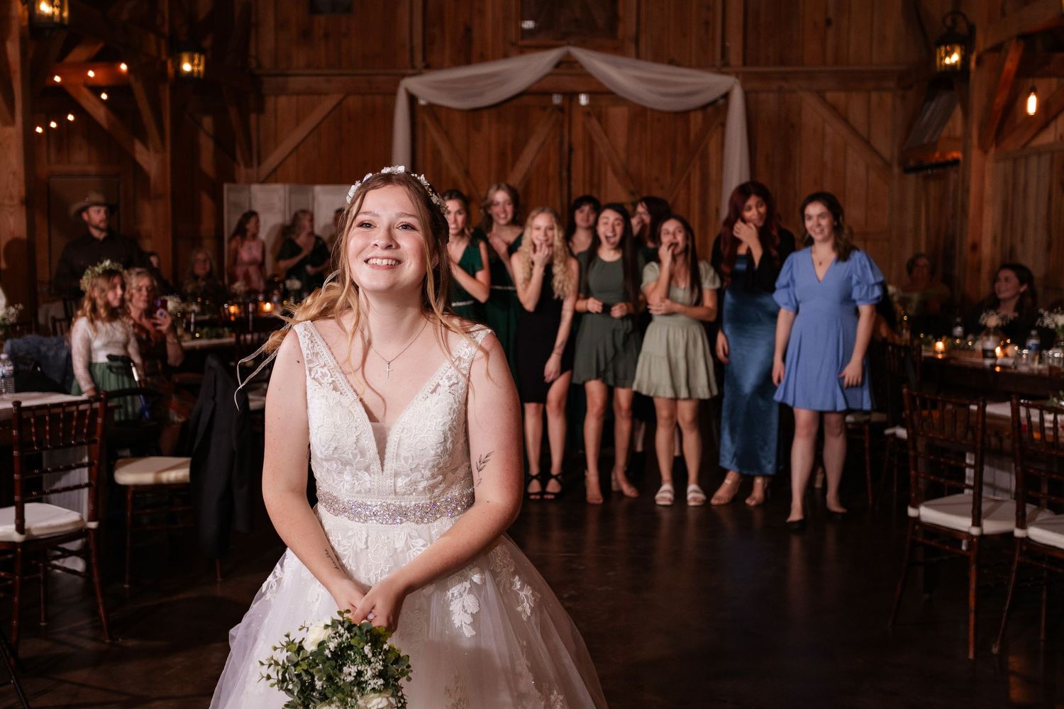 Bridal portrait in rustic barn venue with guests in background.