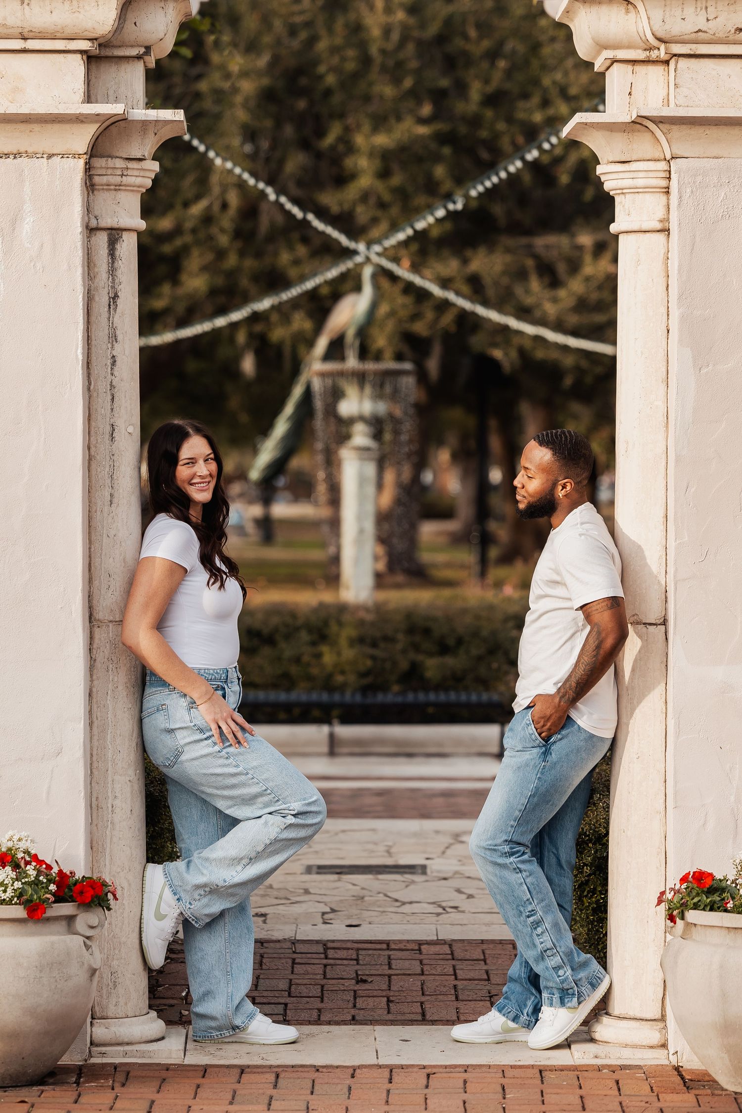 Smiling couple in coordinating white tops and jeans posing on opposite sides of elegant stone arch.