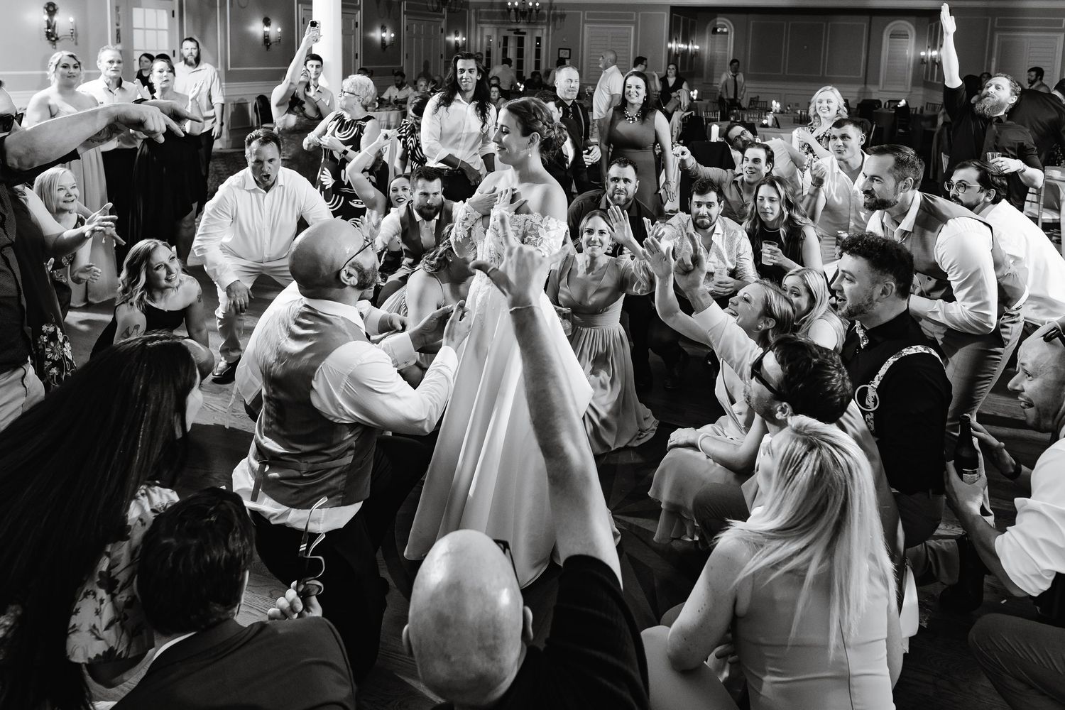 Lively black and white photo of wedding guests dancing together on the reception floor.