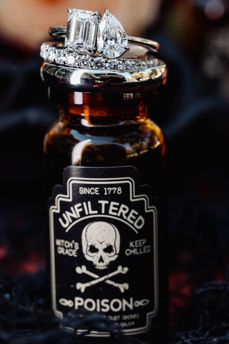 Diamond engagement and wedding rings displayed on gothic skull poison bottle prop.