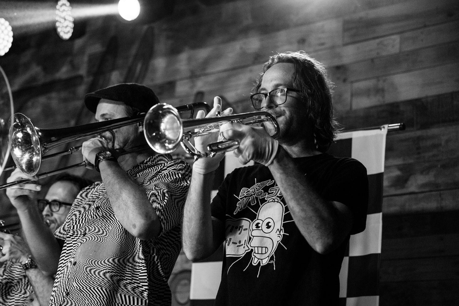 Two trumpet players performing on stage in black and white photo at a live music venue.