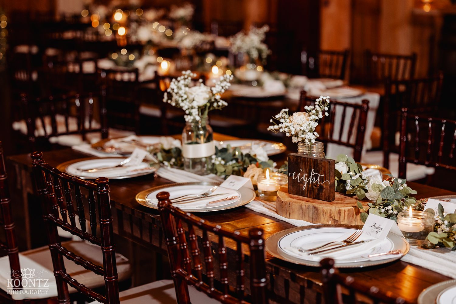 Rustic wedding reception tables decorated with greenery garlands, white flowers, and warm candlelight.