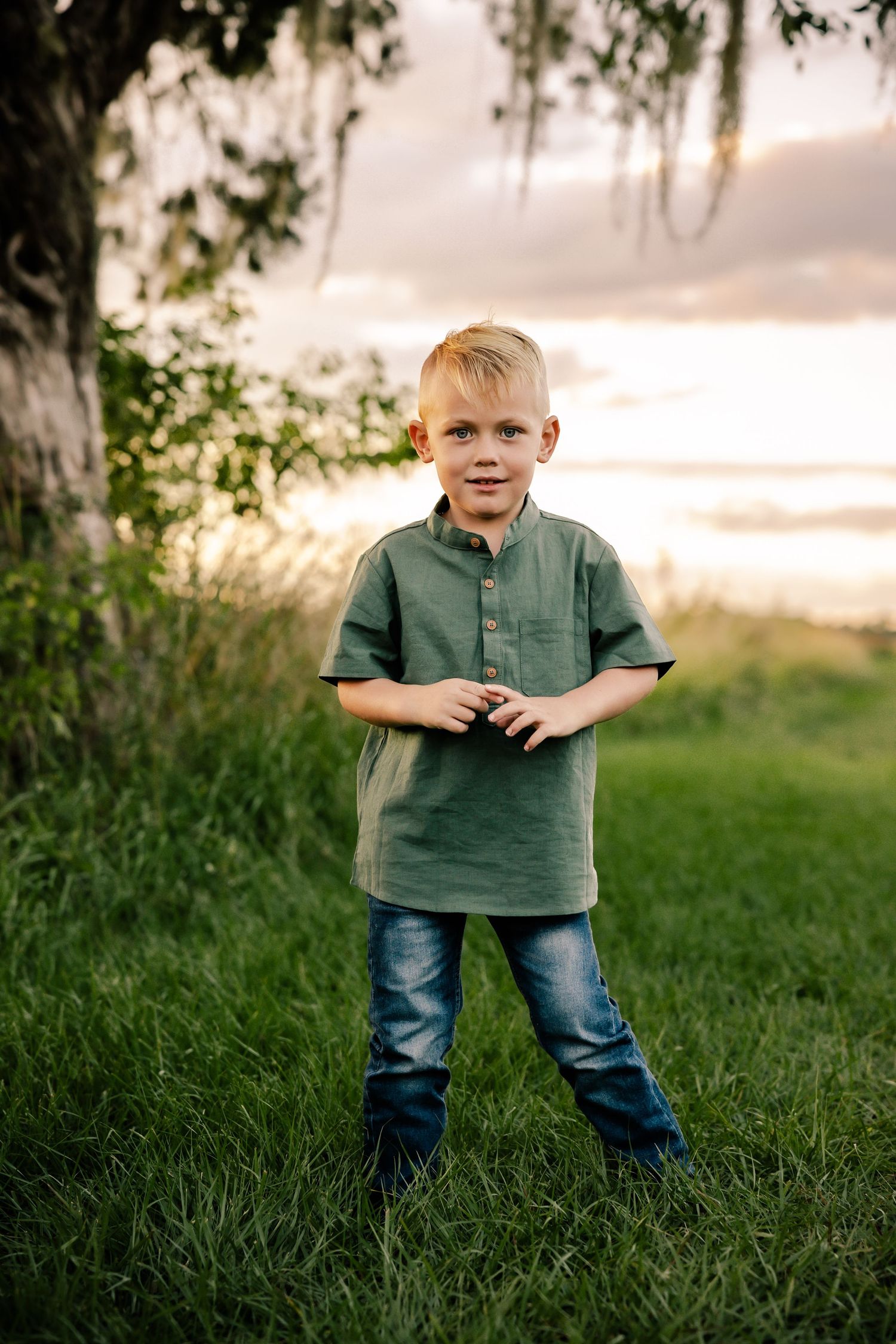 A child stands in green grass wearing casual clothing during golden hour.