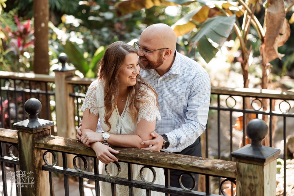 Couple sharing intimate moment while leaning on iron railing in outdoor garden setting.