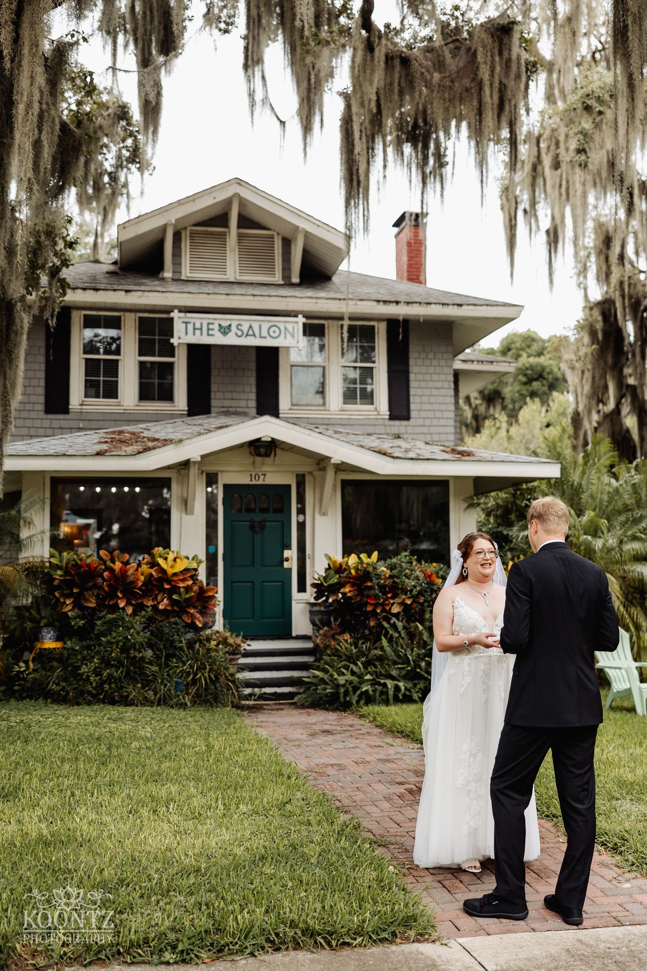 A wedding couple stands on a brick path in front of The Watson House with hanging Spanish moss overhead.