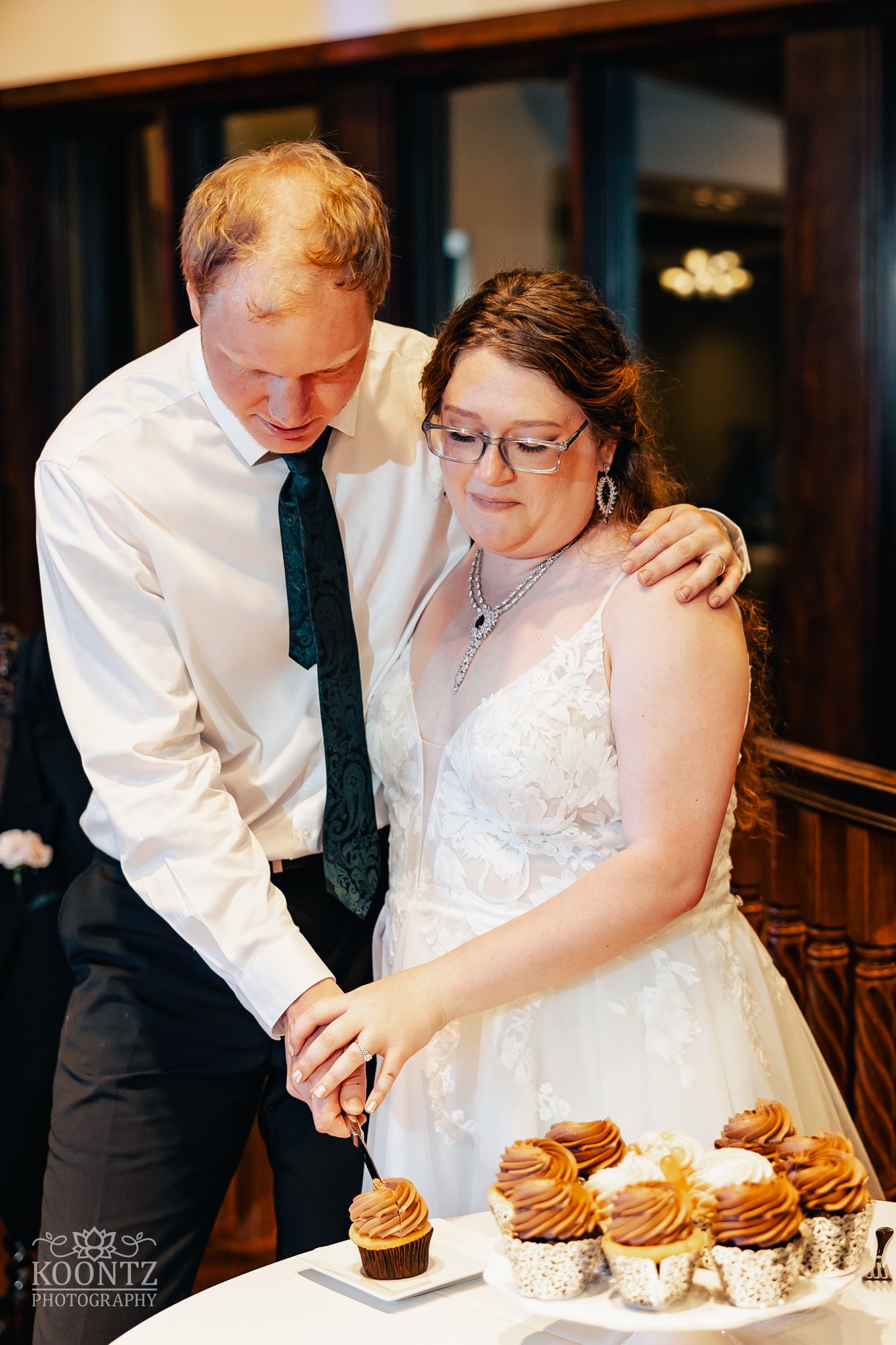 A couple cuts their wedding cupcakes together during their reception celebration.
