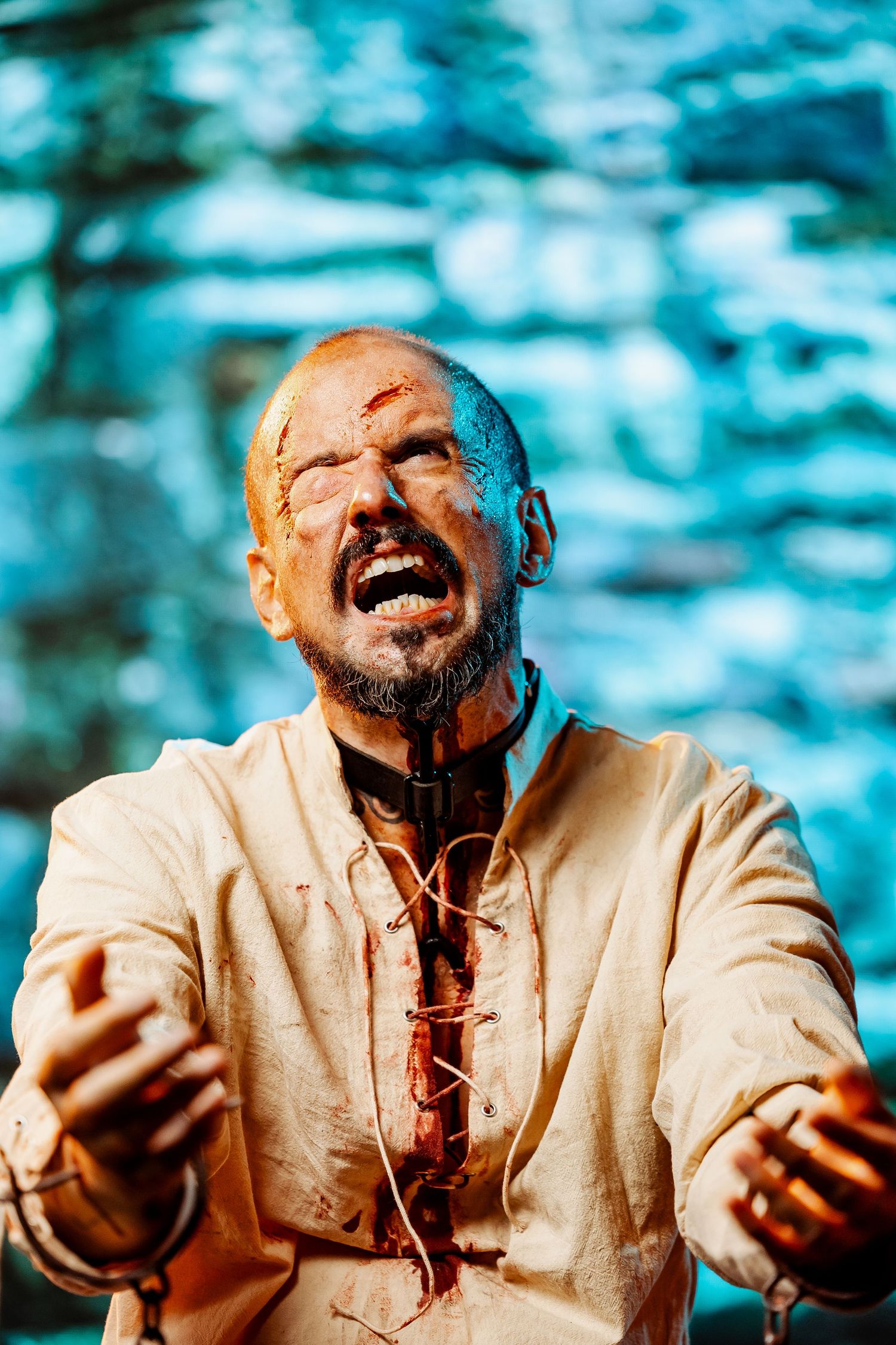 Dramatic theatrical portrait against blue background showing intense emotion and theatrical makeup.