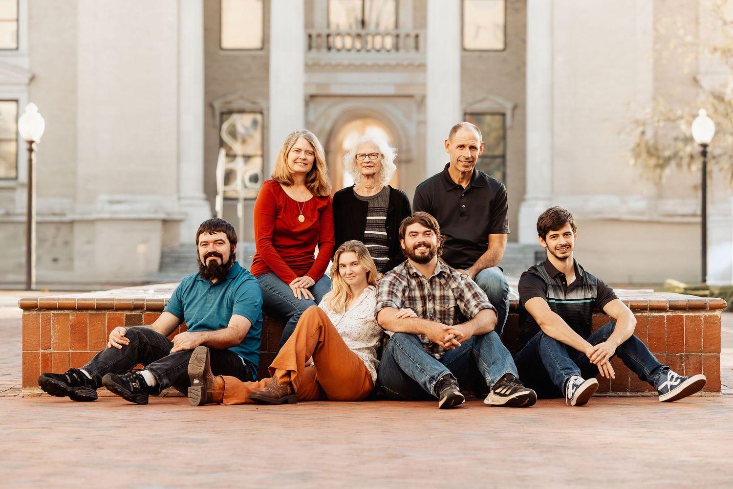 Extended family of seven casually posing on brick steps in front of a building.