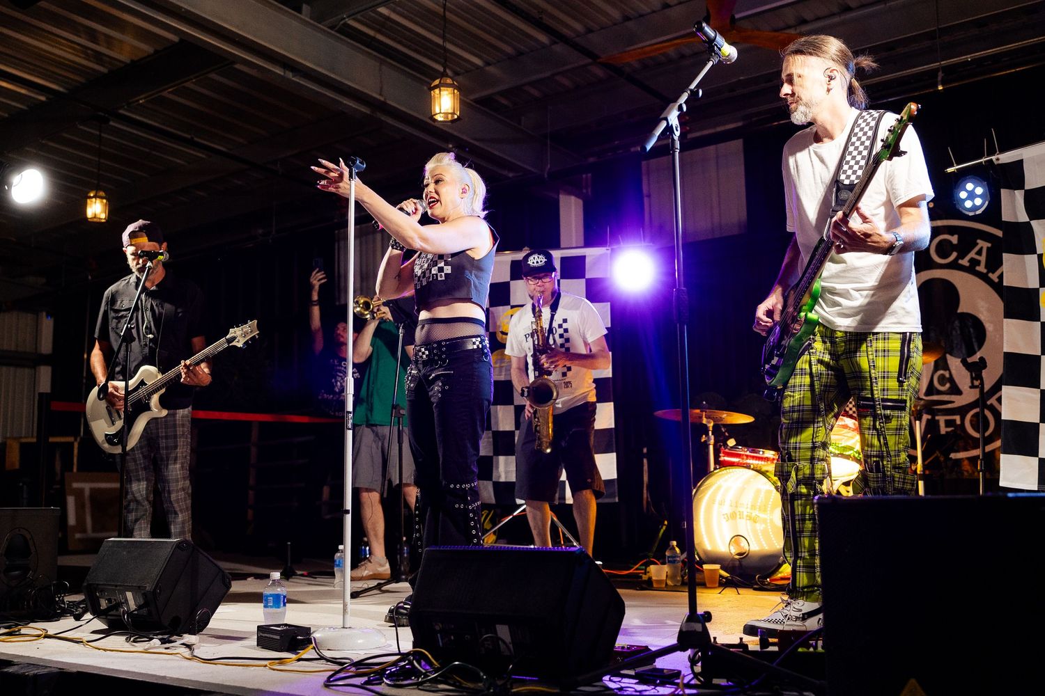 A energetic band performs on an outdoor stage, featuring a female vocalist and guitarist with checkered flag decor.