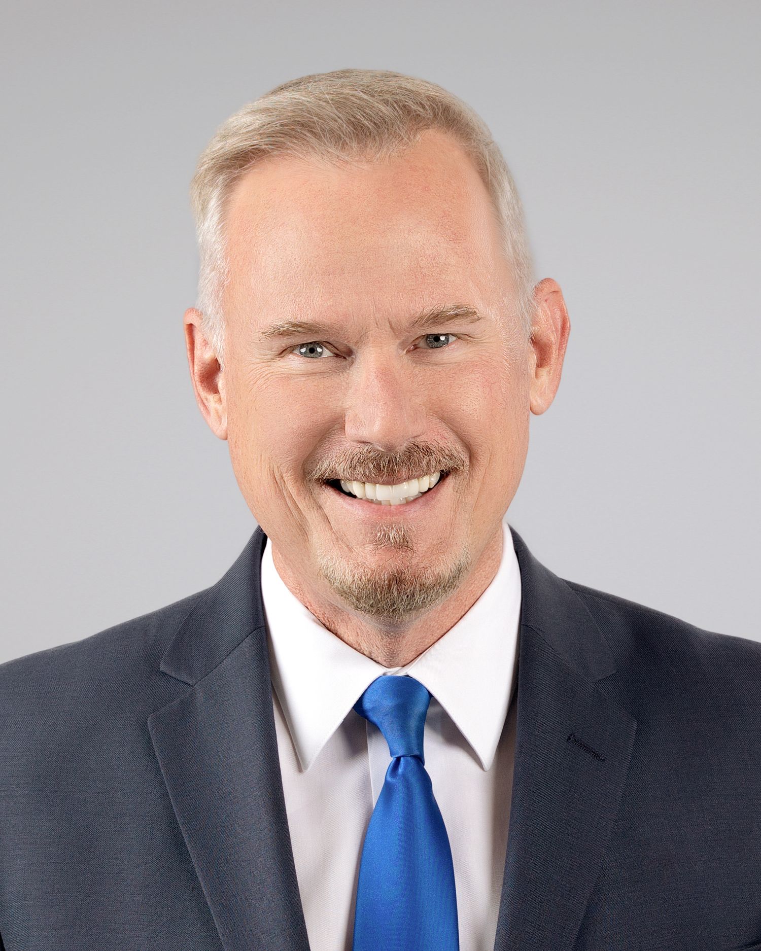 Professional headshot of a smiling man with gray hair wearing a suit and blue tie.