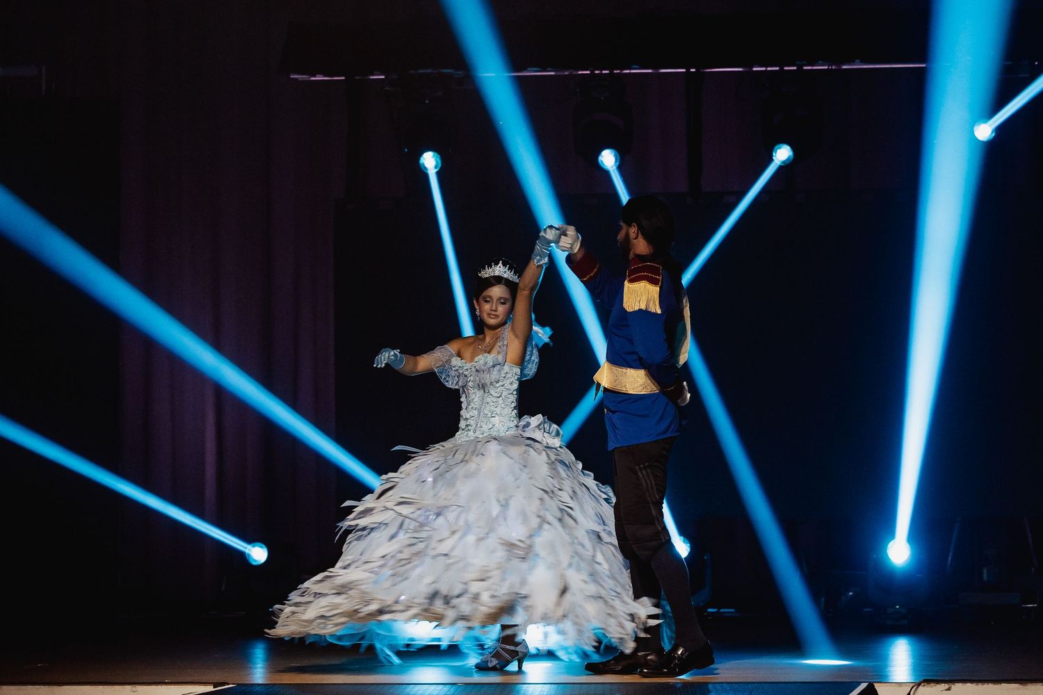 Two performers in princess and prince costumes dancing on a lit stage.