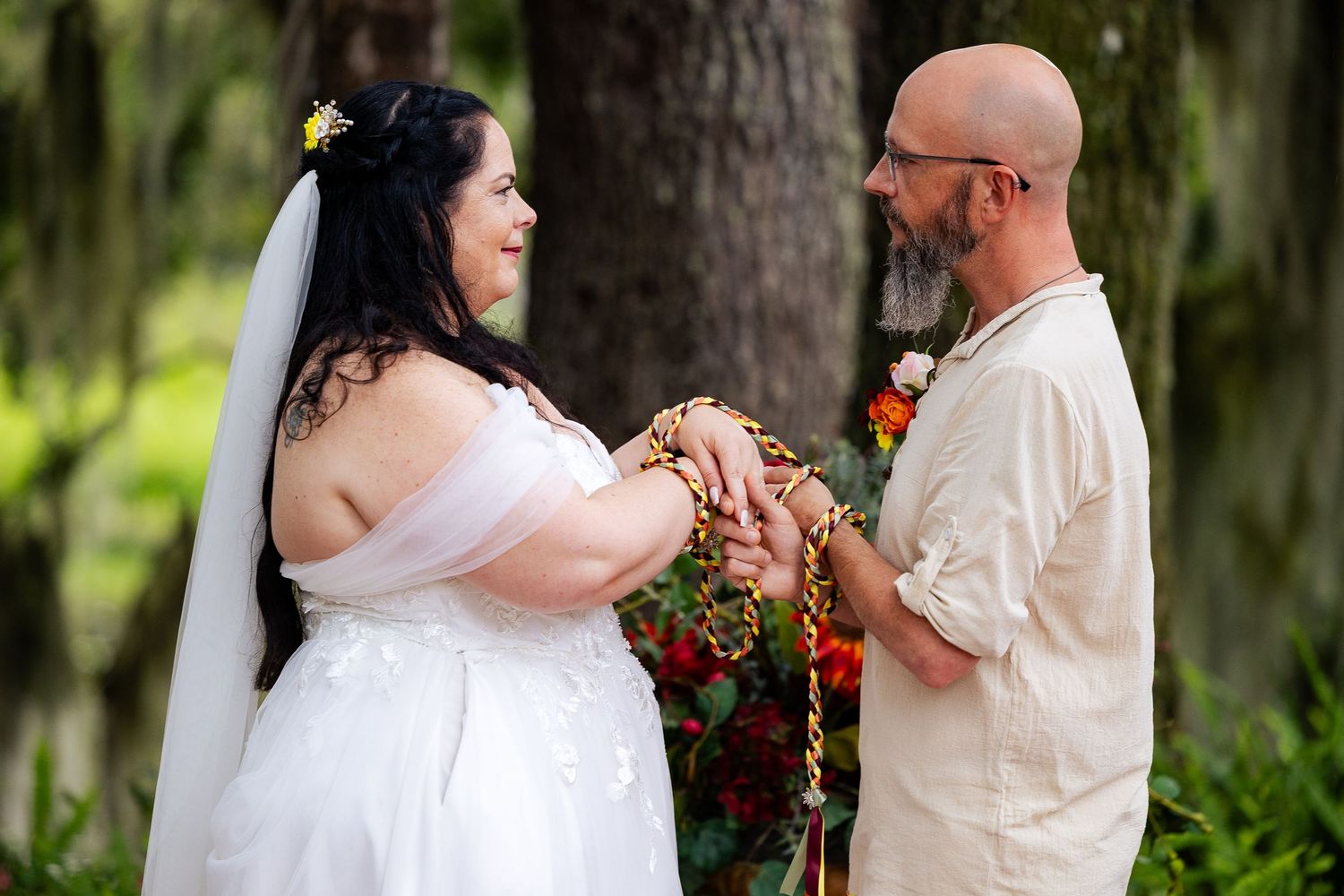 Bride and groom exchange vows during an outdoor woodland handfasting wedding ceremony in a lush forest setting.