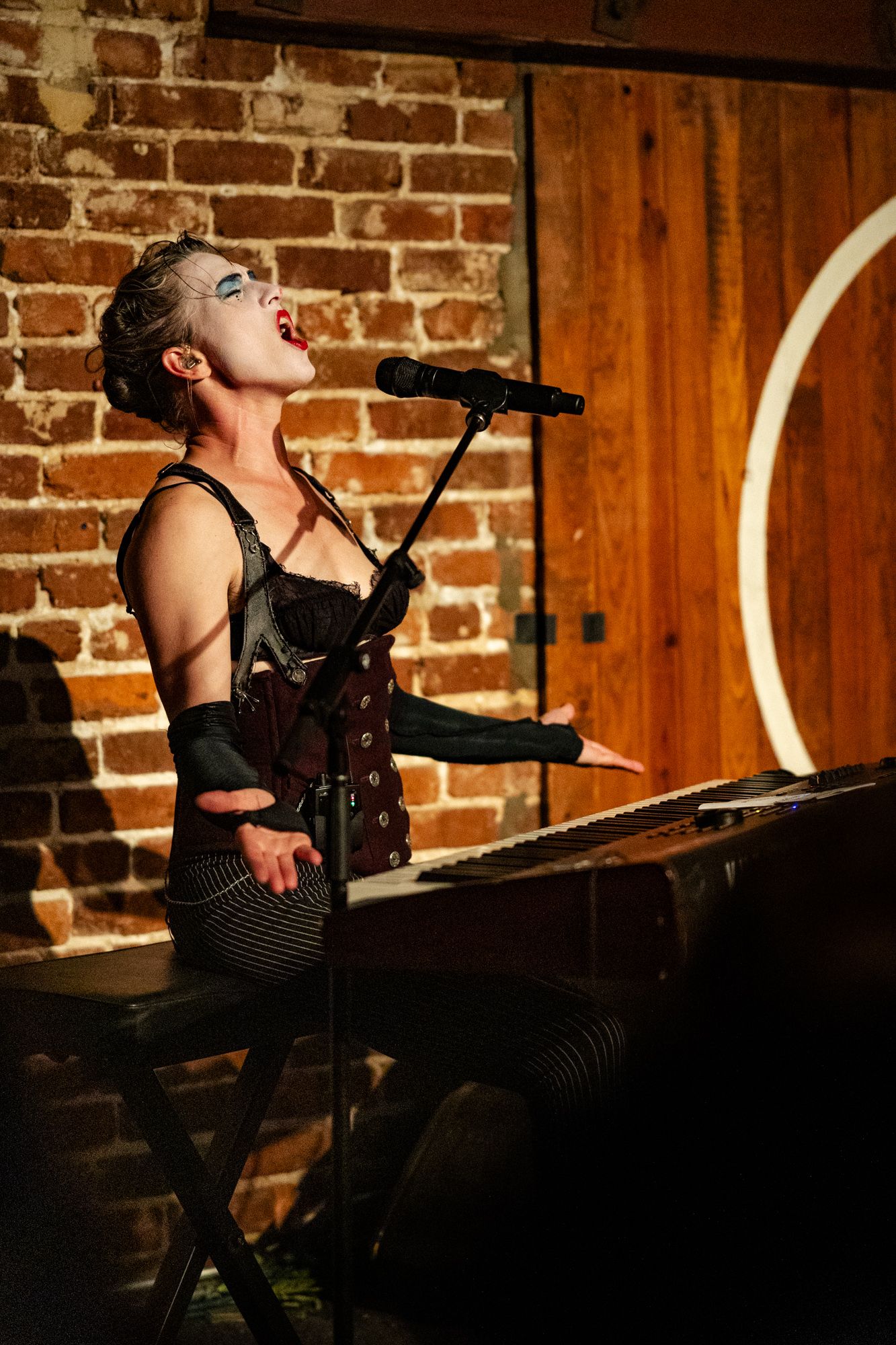 Amanda Palmer, Dresden Dolls, The Social Orlando FL, June 18 2023, singing at keyboard in gothic corset, brick wall background