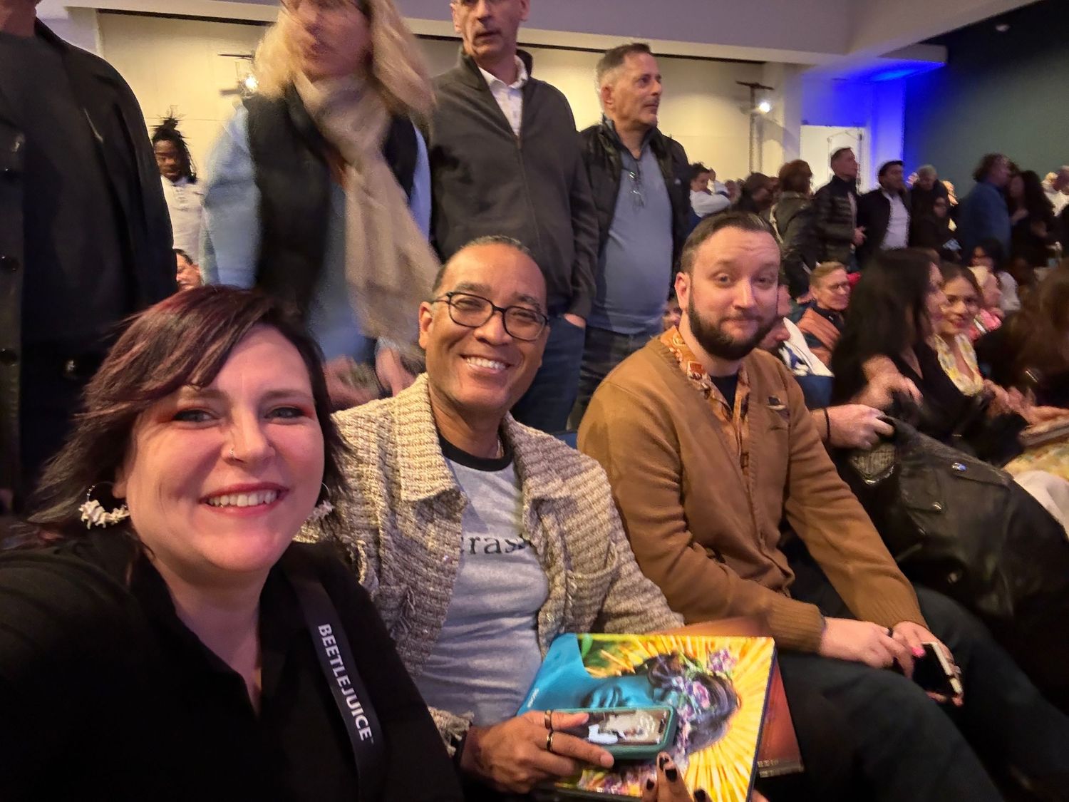 A group of attendees smile while seated at an event, with one person holding a book or program.