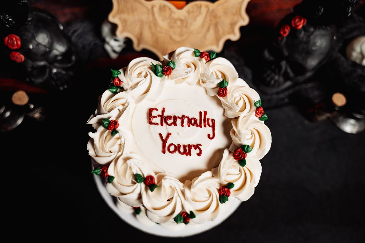 A white frosted cake with red lettering saying 'Eternally Yours' decorated with swirled piping on a dark background.