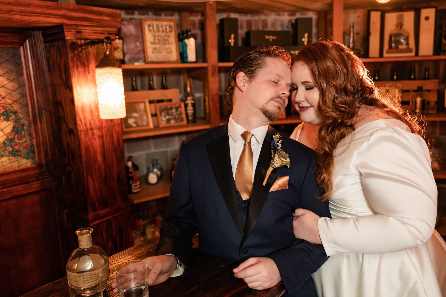 Bride leans on groom's shoulder as they share a warm moment together inside a cozy rustic bar.