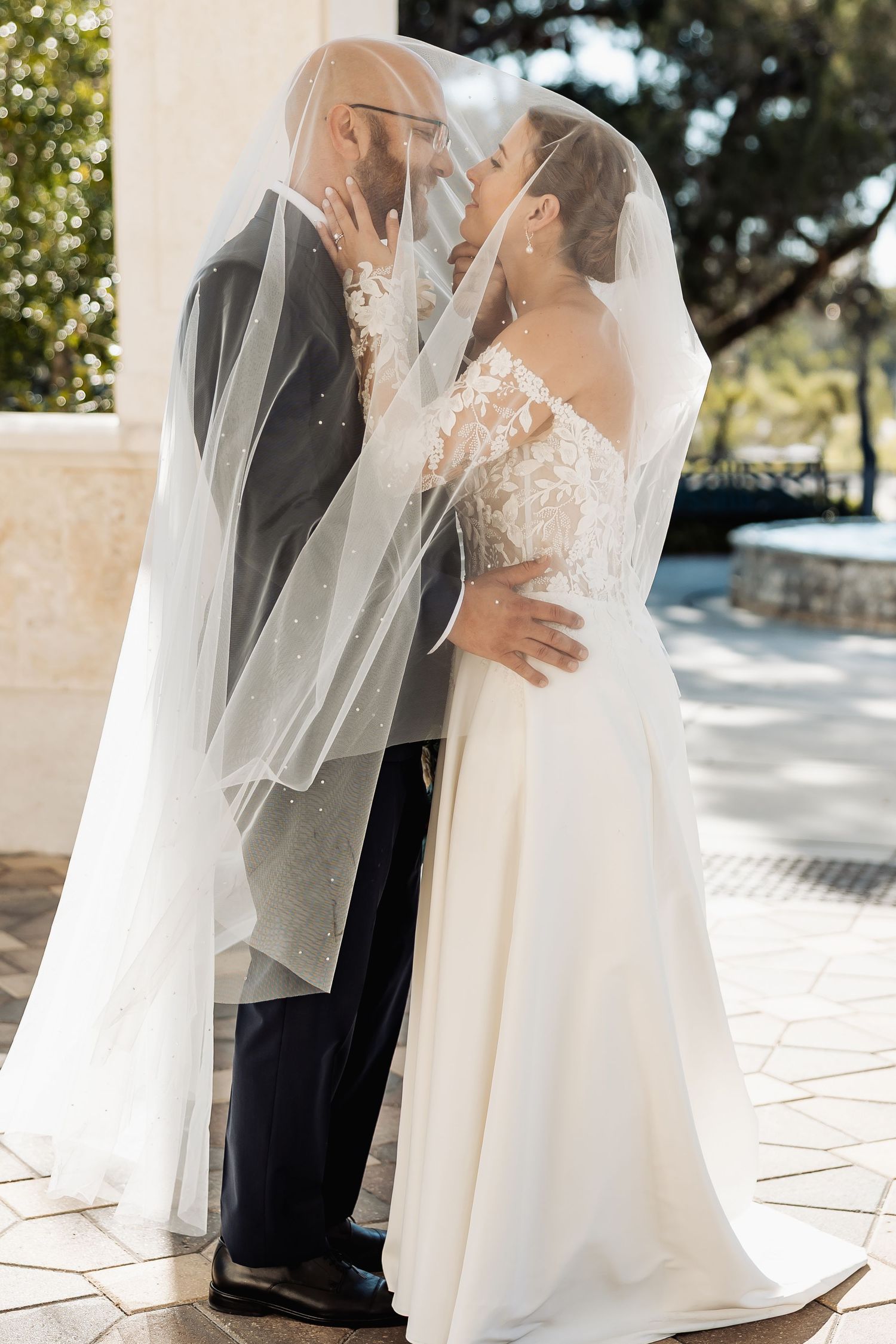 Bride and groom sharing a romantic kiss under a flowing white wedding veil outdoors.
