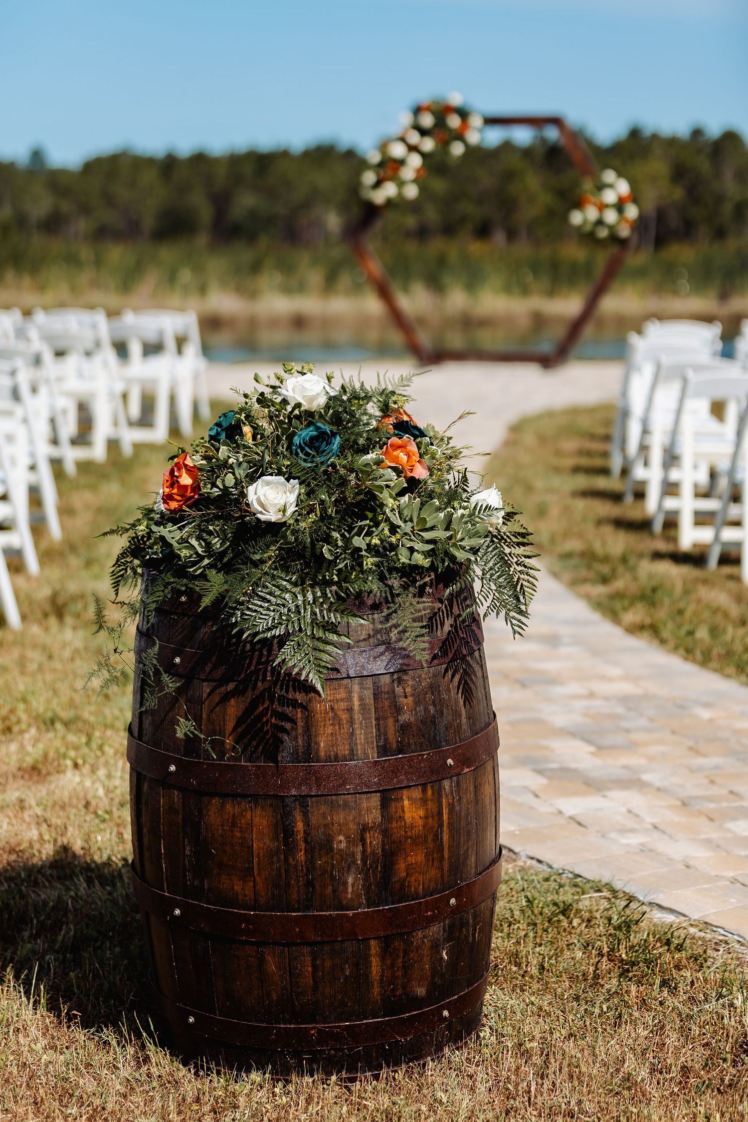 Rustic wooden barrel decorated with floral arrangements at an outdoor wedding ceremony setup.