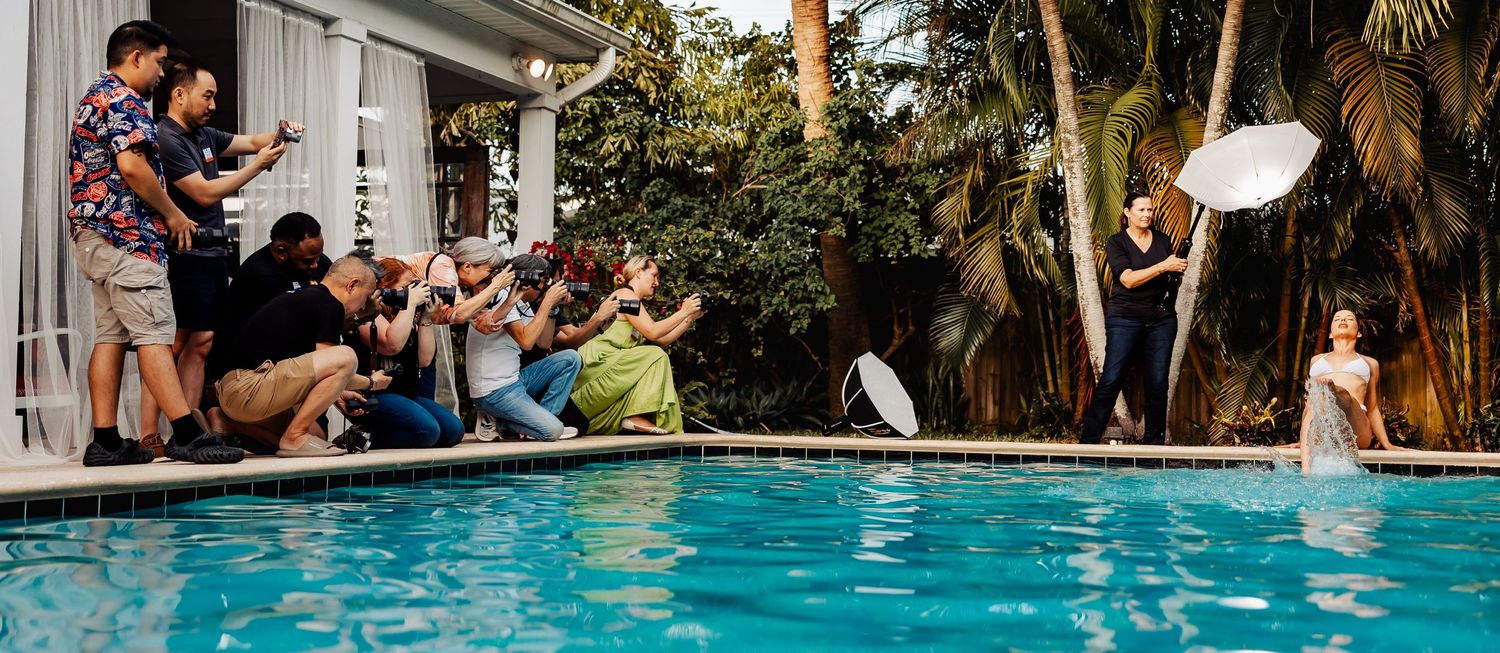 Wide angle view of photographers shooting poolside with palm trees in background.