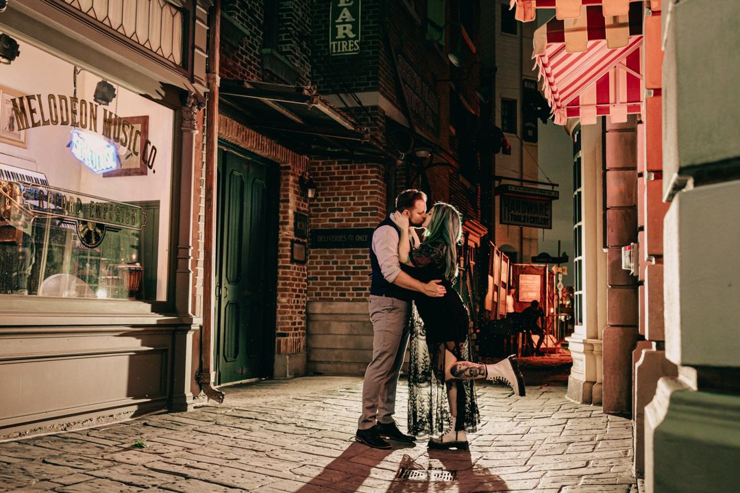 Couple sharing a tender kiss on a cobblestone street beside the Melodeon Museum at night.