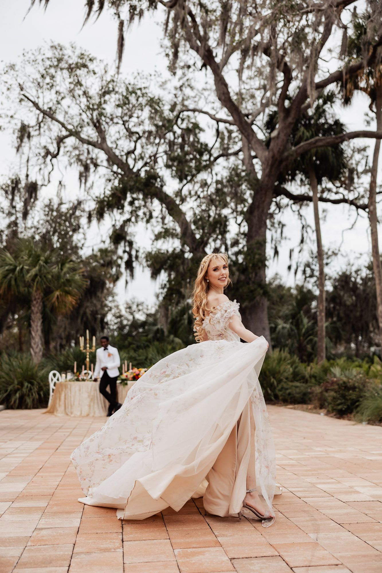 Radiant bride twirling floral wedding gown on outdoor terrace beneath Spanish moss-draped oak trees.