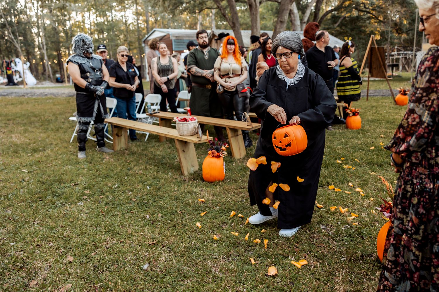 Guests in Halloween costumes play games with jack-o-lantern pumpkins at outdoor fall celebration.