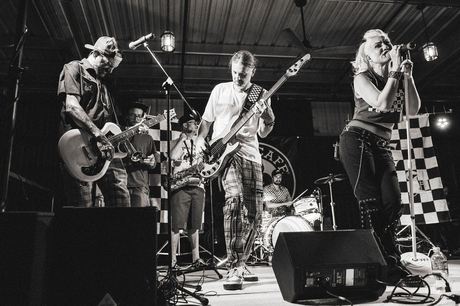 Rock band performs on stage in black and white photo with checkered backdrop.