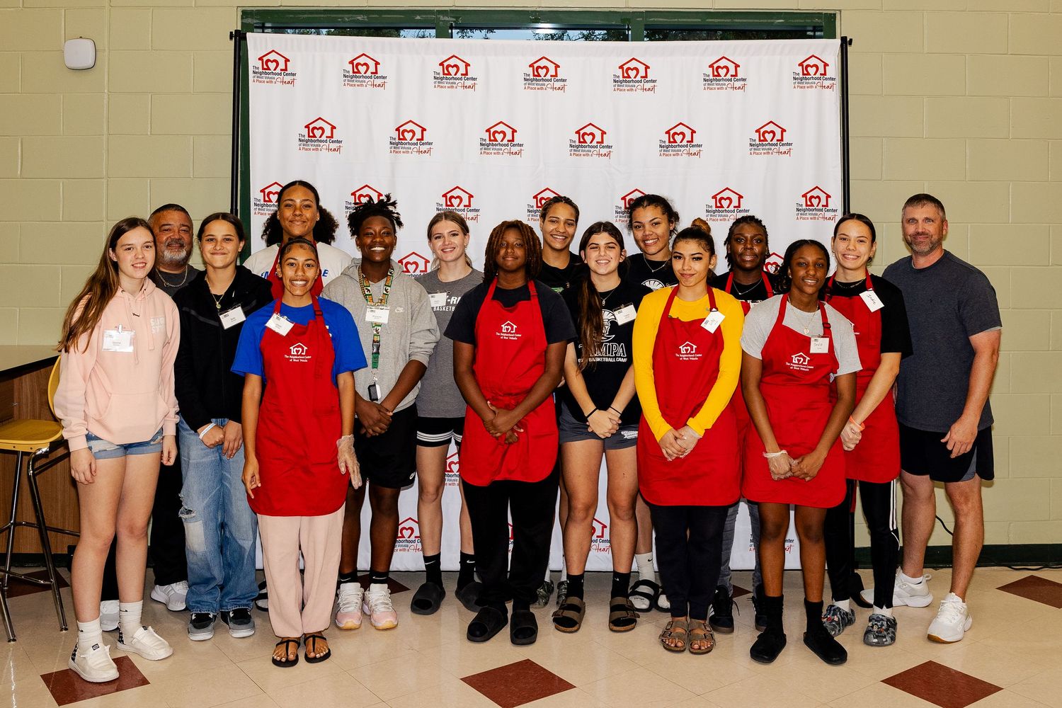 Small group of youth and adult volunteers posing in front of a branded step-and-repeat banner.