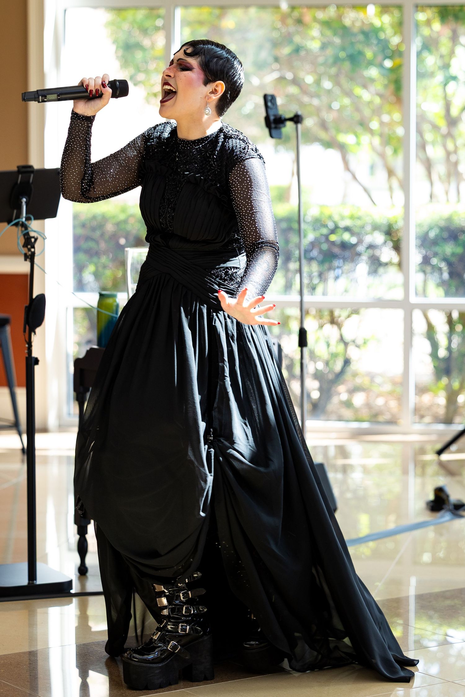 A performer in a black gown sings passionately into a microphone on stage.