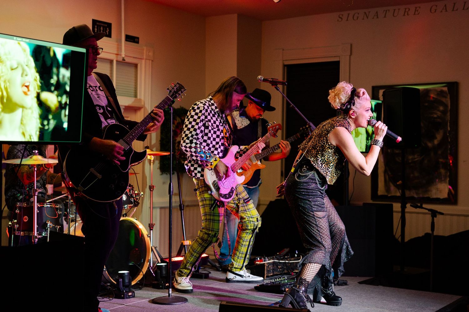 Live band performs on stage with guitarist, bassist, and female vocalist singing passionately under warm stage lights.
