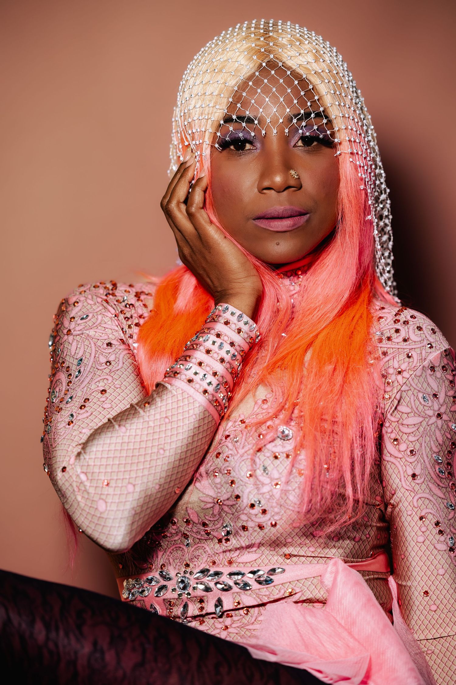Woman with pink-orange ombre hair and jeweled veil poses in a rhinestone-embellished pink outfit.
