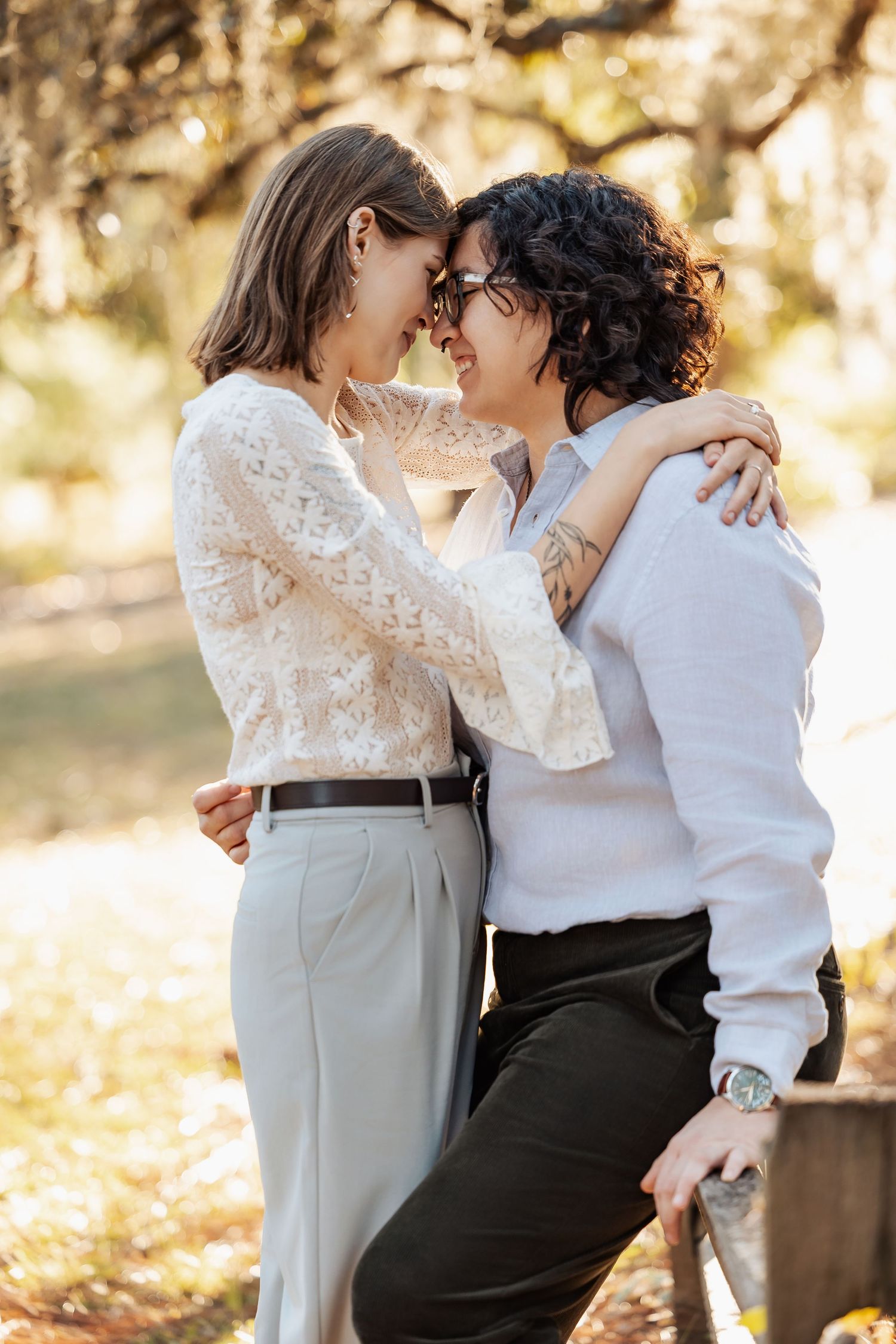 Two women touching foreheads romantically while embracing outdoors in warm autumn sunlight.