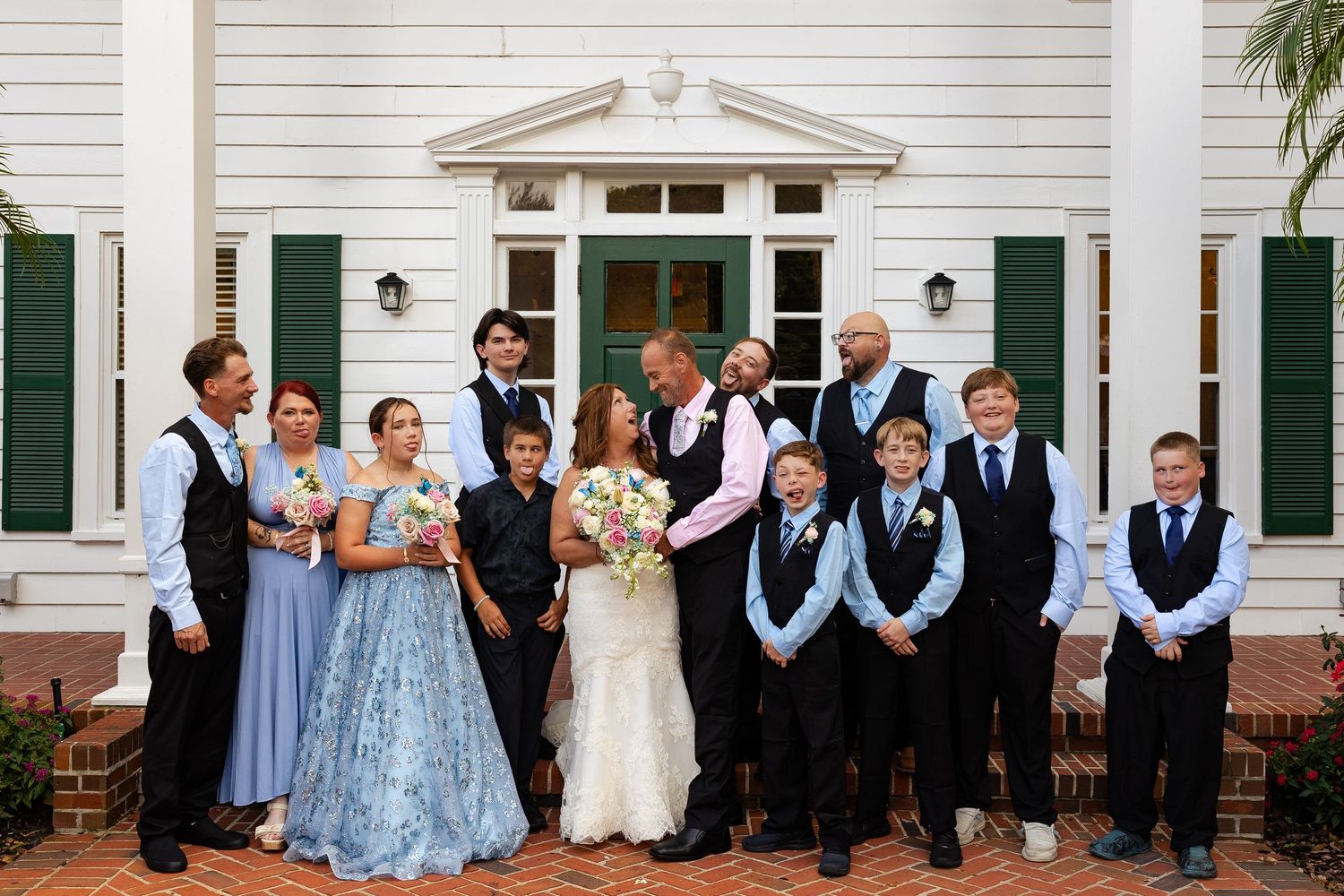Wedding party poses in front of elegant white Southern colonial mansion with green shutters.