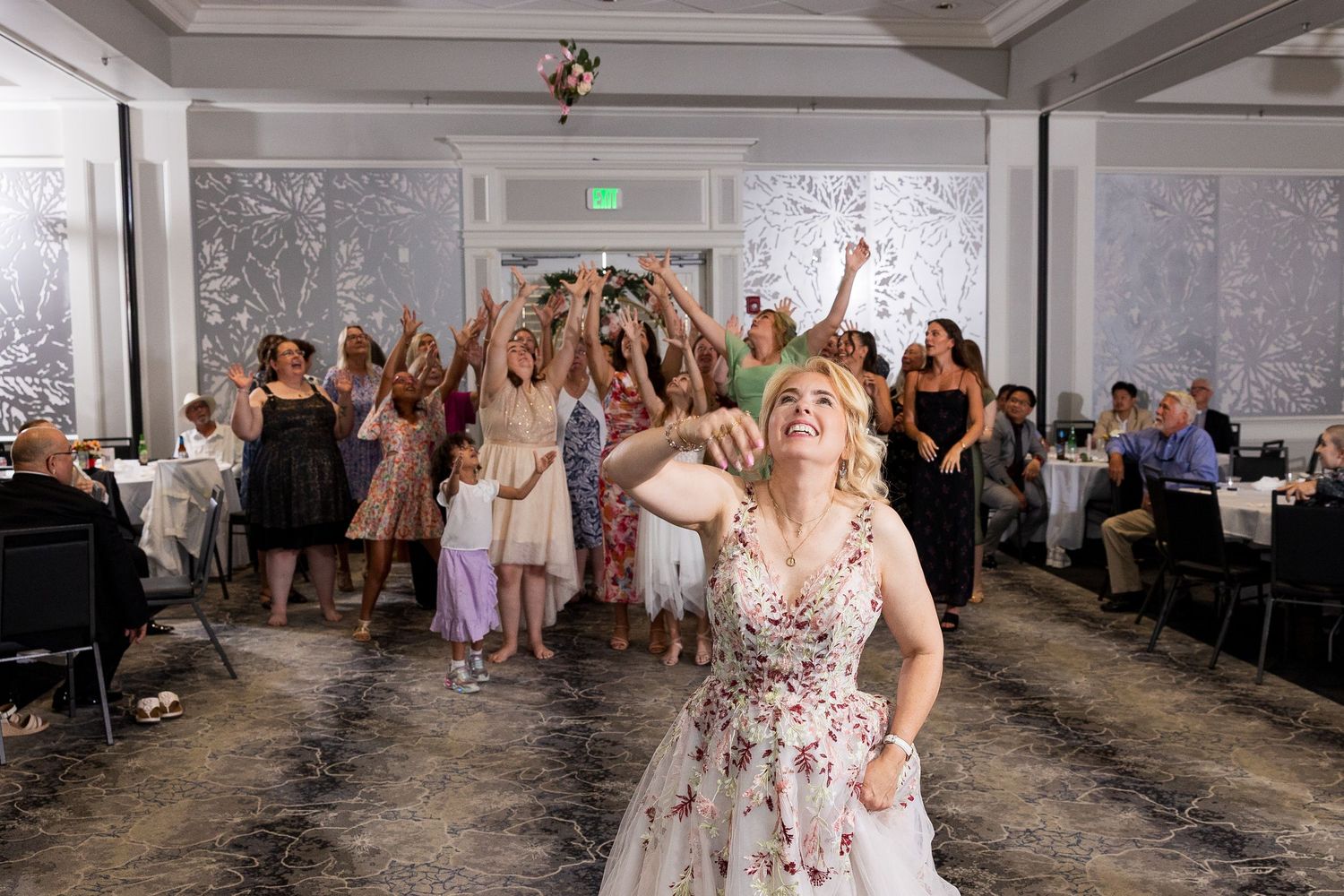 Bride tosses her bouquet to a crowd of eager guests reaching up at the wedding reception.