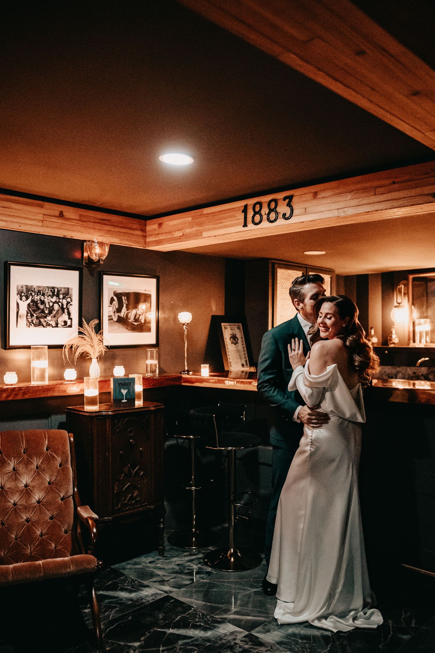 Romantic couple embracing in warmly lit vintage bar with 1883 sign.