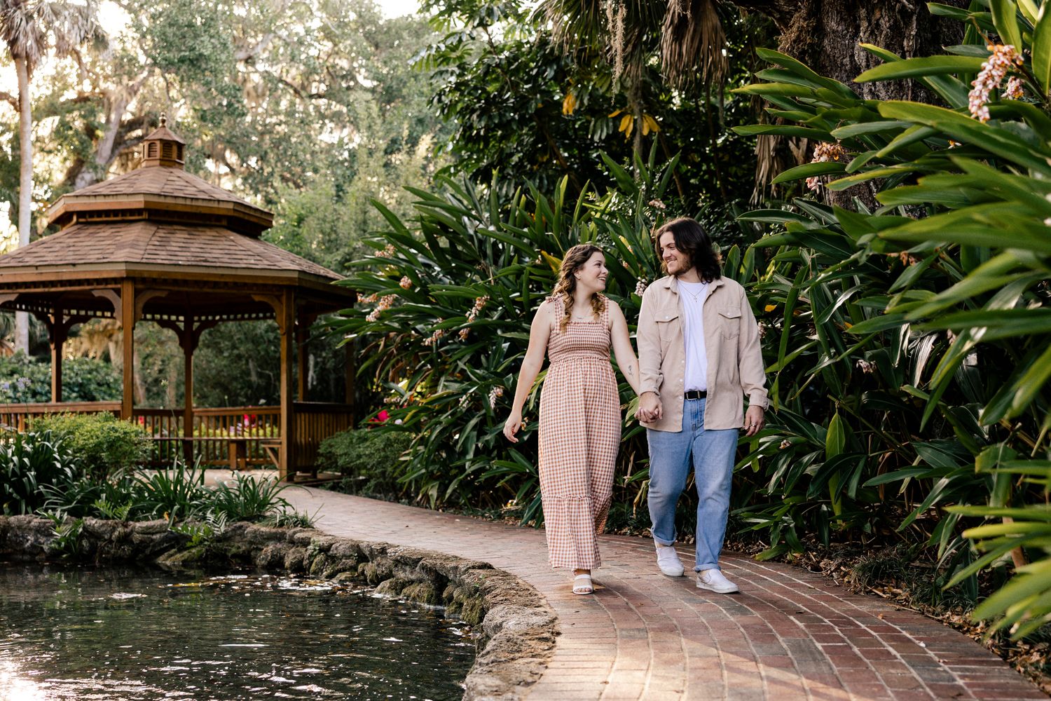 Couple walking together on pathway near tropical garden gazebo.