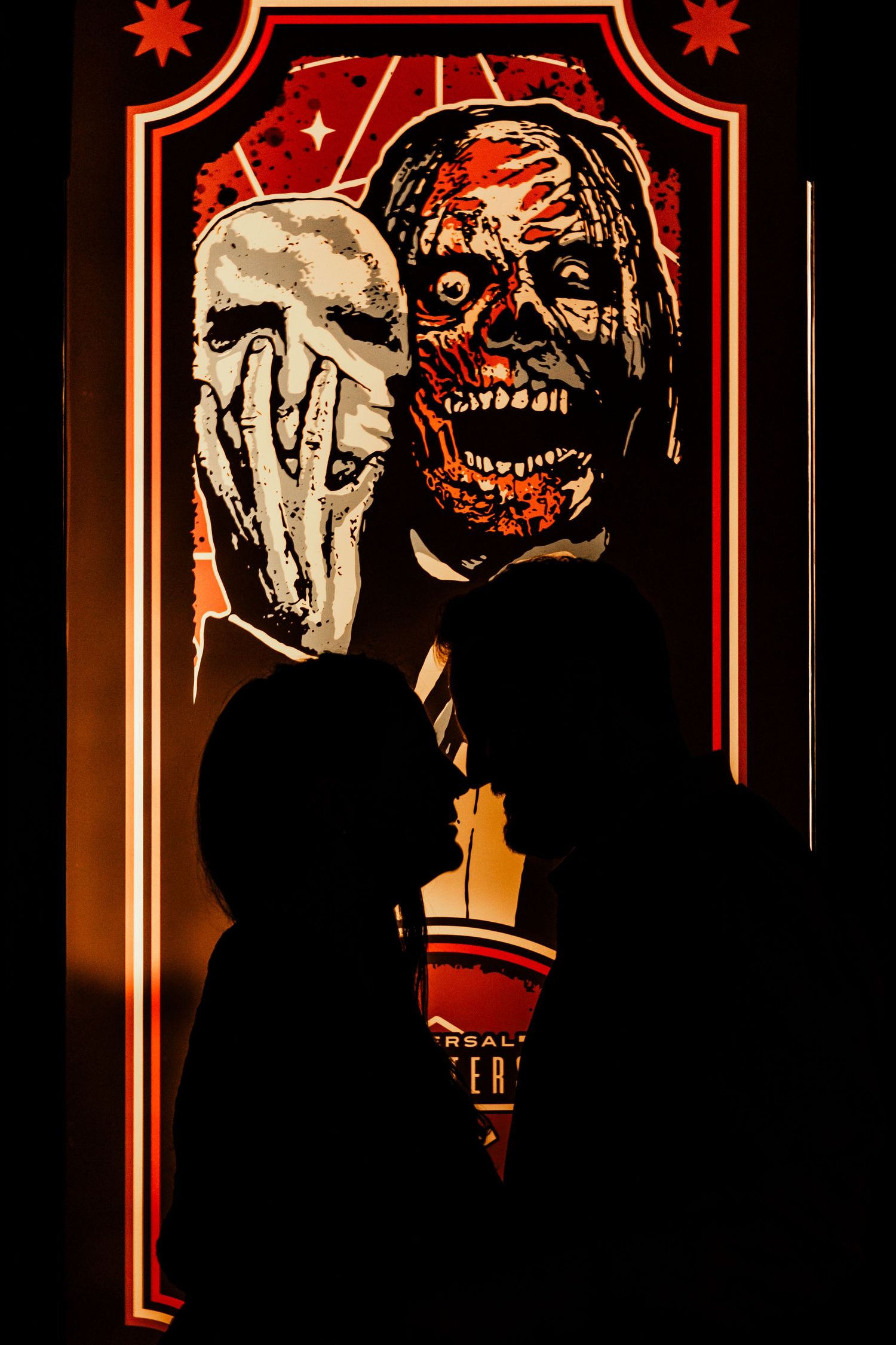 Silhouettes of people against a spooky Halloween horror poster with red lighting and skull artwork.